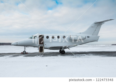 Modern white private jet with an opened gangway door at the winter airport apron 122473348