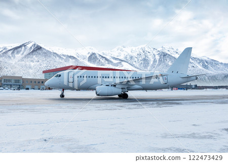 White passenger plane taxiing on the airport at winter on the background of high scenic mountains White passenger plane taxiing on the airport at winter on the background of high scenic mountains 122473429