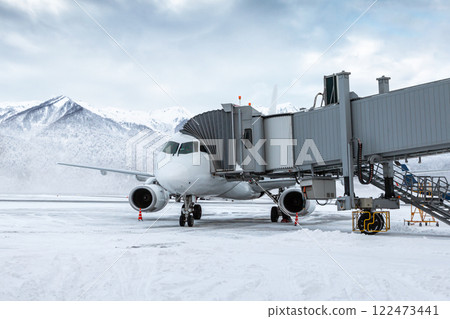 White passenger jet plane at the airgate at winter airport apron on the background of high picturesque mountains White passenger jet plane at the airgate at winter airport apron on the background of high picturesque mountains 122473441