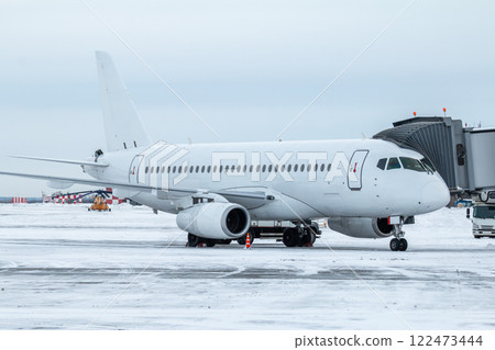 White passenger jet plane at the boarding bridge at winter airport apron White passenger jet plane at the boarding bridge at winter airport apron 122473444