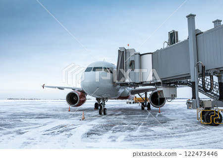 Passenger airplane at the airbridge at winter airport apron 122473446