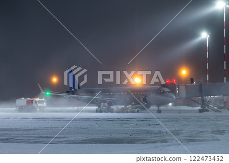 Ground handling of a passenger aircraft at the air bridge in a winter blizzard at night Ground handling of a passenger aircraft at the air bridge in a winter blizzard at night 122473452