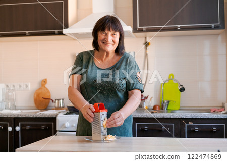 Woman is smiling while using a food grater in a kitchen Woman is smiling while using a food grater in a kitchen 122474869
