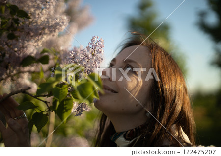 Joyful woman enjoying the fragrance of lilac blossoms in a serene garden on a sunny spring day Joyful woman enjoying the fragrance of lilac blossoms in a serene garden on a sunny spring day 122475207
