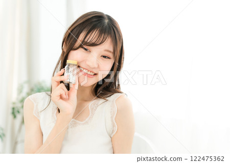 微笑的亞洲女人拿著一瓶藥/補品 微笑的亞洲女人拿著一瓶藥/補品 122475362