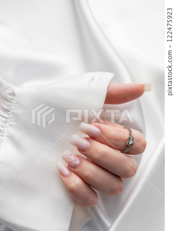 Woman showing stylish pastel pink manicure and silver ring on white silk fabric Woman showing stylish pastel pink manicure and silver ring on white silk fabric 122475923