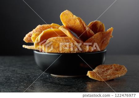 Dried mango slices in a black dish on a black background. 122476977