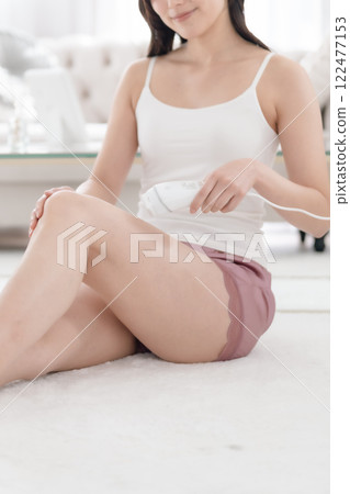 Young woman applying light hair removal to her legs, no face Young woman applying light hair removal to her legs, no face 122477153