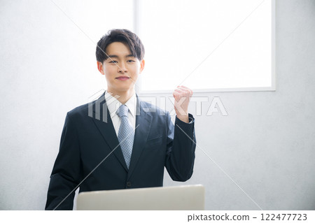 A young man in a business suit making a fist pump in front of a beautiful backlit window. Image for recruitment, presentation, etc. A young man in a business suit making a fist pump in front of a beautiful backlit window. Image for recruitment, presentation, etc. 122477723
