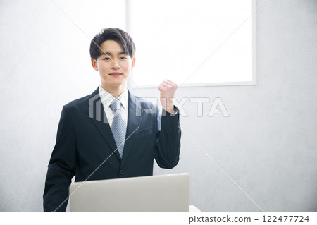 A young man in a business suit making a fist pump in front of a beautiful backlit window. Image for recruitment, presentation, etc. A young man in a business suit making a fist pump in front of a beautiful backlit window. Image for recruitment, presentation, etc. 122477724