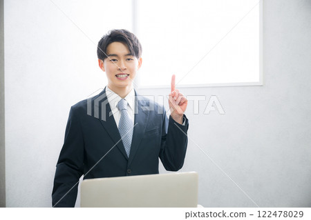 A young man in a business suit posing point-like by a beautiful backlit window, looking at the camera A young man in a business suit posing point-like by a beautiful backlit window, looking at the camera 122478029