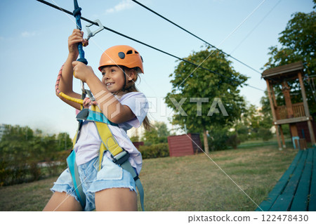 Happy girl child going down zipline inclined rope with a suspended harness Happy girl child going down zipline inclined rope with a suspended harness 122478430
