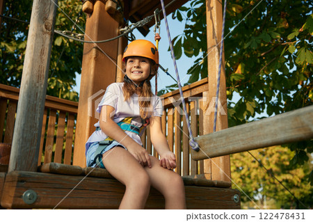Relaxed girl child sitting on wooden rope playground taking break Relaxed girl child sitting on wooden rope playground taking break 122478431