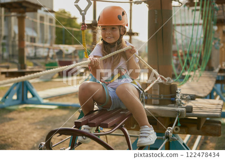 Playful little girl child pulling hawser while overcoming obstacles at rope park 122478434