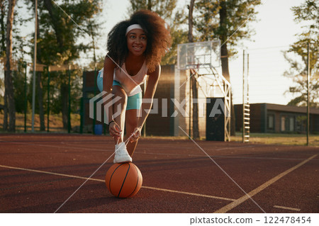 Female basketball player tying shoelaces putting foot on ball Female basketball player tying shoelaces putting foot on ball 122478454