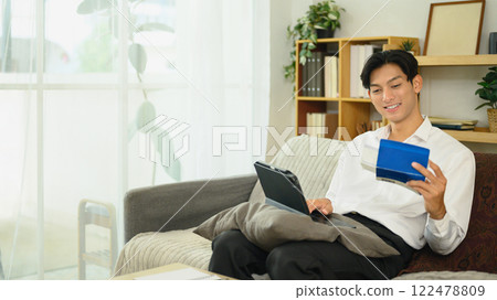 Smiling asian man holding a savings passbook and checking his financial transactions on digital tablet 122478809
