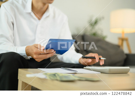 Young adult man using calculator while managing his home finances on the table 122478842