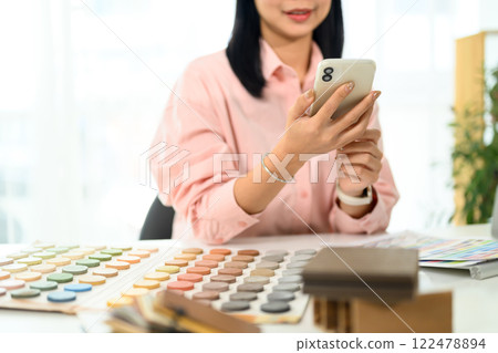 Smiling creative woman reviewing design inspirations on her smartphone at office desk 122478894