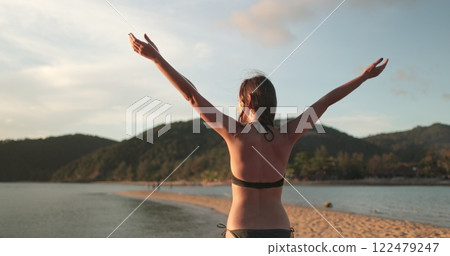 Woman in bikini is relax sandy beach of Koh Ma Beach on Koh Phangan Island in Thailand, enjoying the tropical evening sunset. Outdoor lifestyle travel on summer holiday vacation. Back view 122479247