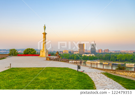 The Victor Monument stands tall at Kalemegdan Fortress in Belgrade, overlooking the city as the sun sets, casting warm colors across the sky and reflecting on the river below. 122479353