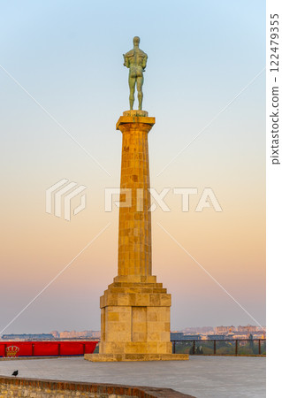 The majestic Victor Monument stands tall at Kalemegdan Fortress, silhouetted against a colorful sunset sky in Belgrade, symbolizing triumph and history at this significant location. 122479355
