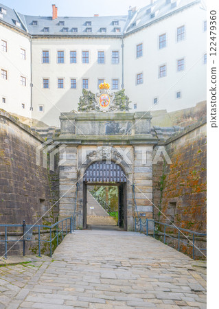 The majestic main entrance gate of Konigstein Fortress, located in Saxony, Germany, welcomes visitors with its impressive stone architecture and rich history. 122479360