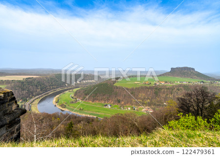 From the heights of Konigstein Fortress, the Elbe River elegantly winds through the lush Saxon landscape, showcasing verdant hills and distant cliffs under a clear sky. 122479361