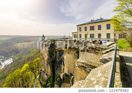 Visitors stroll along the edge of Konigstein Fortress in Saxony, enjoying breathtaking views of the surrounding landscape under a bright, sunny sky. 122479362