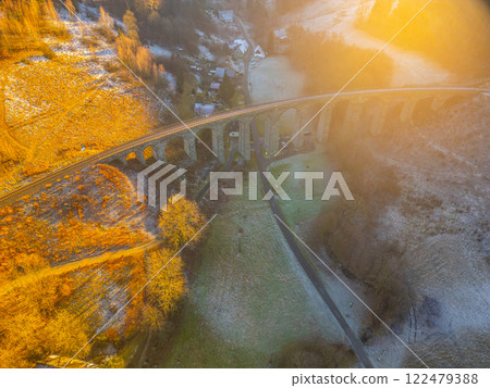 A railway stone bridge spans across a scenic valley in Novina during a beautiful winter sunset. The landscape is lit with warm golden hues, enhancing the tranquil atmosphere. A railway stone bridge spans across a scenic valley in Novina during a beautiful winter sunset. The landscape is lit with warm golden hues, enhancing the tranquil atmosphere. 122479388
