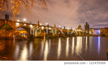 Illuminated by streetlights, Charles Bridge spans over the Vltava River, reflecting its lights on the water. Evening clouds float above the historic architecture of Prague. Illuminated by streetlights, Charles Bridge spans over the Vltava River, reflecting its lights on the water. Evening clouds float above the historic architecture of Prague. 122479389