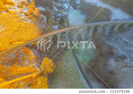 A beautiful winter sunset casts golden hues over the railway stone bridge in Novina, Krystofovo udoli. The surrounding landscape features a serene atmosphere with frost-covered fields. A beautiful winter sunset casts golden hues over the railway stone bridge in Novina, Krystofovo udoli. The surrounding landscape features a serene atmosphere with frost-covered fields. 122479396