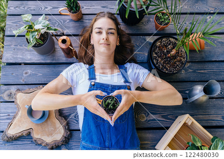 An overhead shot of happy woman enjoy her hobby lying on wooden terrace covered with potted plants, a watering can and gardening equipment. 122480030