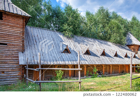 Wooden structures bask in sunlight near lush green trees in a serene landscape 122480062