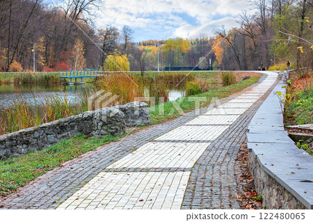 Walking along the tranquil lakeside path surrounded by autumn colors and gentle clouds 122480065