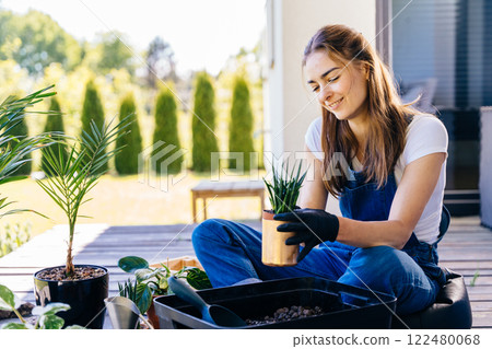 Professional lovely female enjoy her hobby gardening at terrace outdoor holds small pot with succulent with happy face expression in sunny spring day. 122480068