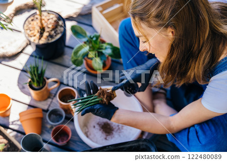 An overhead shot of woman taking care of her houseplants sitting on terrace in sunny day outdoor with smile, replanting succulents in bigger pots. Gardening, plant lover, leisure concept. 122480089