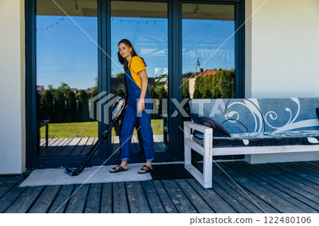 Full height woman housewife using vacuum cleaner on terrace of her house cleaning rug. Full height woman housewife using vacuum cleaner on terrace of her house cleaning rug. 122480106