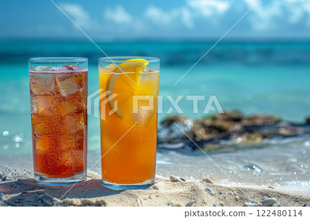 two different cocktails stand in the sand on the edge of the water on a perfect beach in the sand against the backdrop of the blue ocean. 122480114