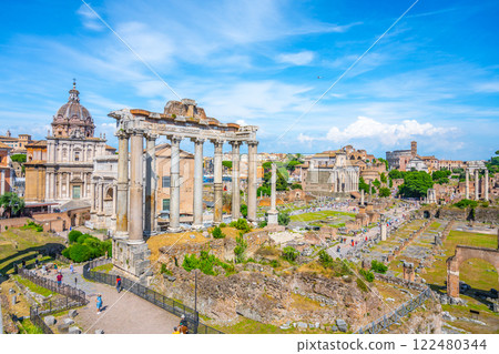 The remnants of the Saturn Temple stand prominently in the Roman Forum, surrounded by ancient structures and vibrant visitors, showcasing the rich history of Rome under clear blue skies. The remnants of the Saturn Temple stand prominently in the Roman Forum, surrounded by ancient structures and vibrant visitors, showcasing the rich history of Rome under clear blue skies. 122480344