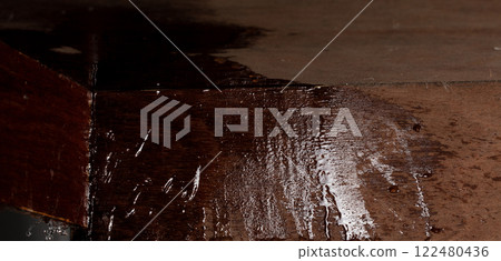 Heavy rain caused ceiling to leak, and big water stain on wooden board. Raindrops were dripping through hole in roof, forming a small leak on ceiling floor. 122480436