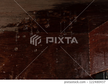 Heavy rain caused ceiling to leak, and big water stain on wooden board. Raindrops were dripping through hole in roof, forming a small leak on ceiling floor. 122480437