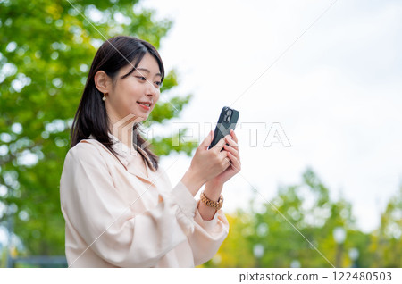 背景有樹木的日本女性操作智慧型手機 背景有樹木的日本女性操作智慧型手機 122480503