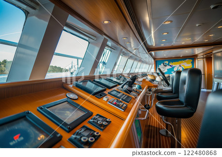 Well lit and spacious cruise ship's bridge with navigational controls, comfy seats, and ocean views from panoramic windows 122480868