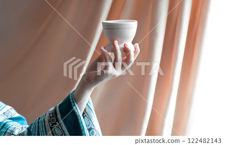 A hand in ancient clothing holds a clay bowl 122482143
