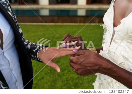 Ambiguous gender fluid couple in white dress, bold suit exchange rings at tropical villa. Fresh lgbtq wedding setting. The bride elegance meets groom style. 122482247
