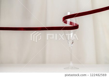 A minimalist and creative composition featuring a wine glass, red velvet ribbon on a soft cream background, representing elegance, Valentines celebration, and sophisticated design. 122482569