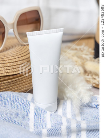 Sunscreen cream tube on bag near towel, dryed grass and sunglasses closeup, cosmetic mockup 122482698