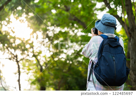 Portrait of Asian mature woman holding a camera and backpack behind her back, an Asia active senior woman enjoying nature in park. Standing on a trail in a forest outdoors. Enjoying active travel trip Portrait of Asian mature woman holding a camera and backpack behind her back, an Asia active senior woman enjoying nature in park. Standing on a trail in a forest outdoors. Enjoying active travel trip 122485697