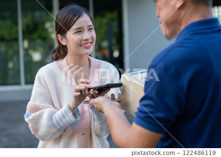 Cheerful Asian women receive product box from delivery service and pays by scanning QR code from smartphone, home deliveries, a convenient shopping experience, and trustworthy doorstep service concept 122486119
