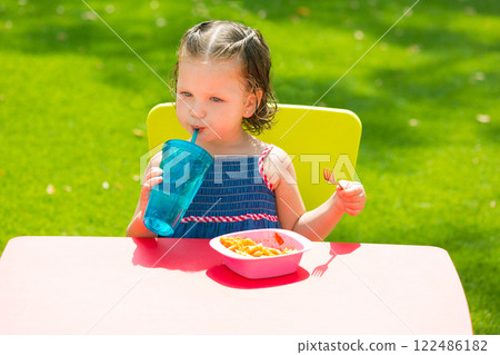 Toddler kid girl drinking eating pasta in garden Toddler kid girl drinking eating pasta in garden 122486182